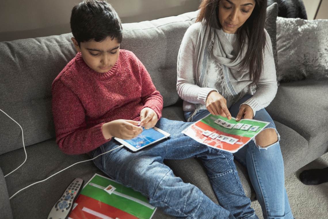 Mother and son sitting on couch using iPad and educational magazine.