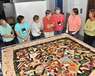 Members of the Michigan Quilt Network view quilts from the MSU Museum's quilt collection. Folk arts curator Marsha MacDowell (far right) and collections assistant Beth Donaldson (next to MacDowell) explain that the quilt was made by Lois Darcus, of Elsie, Michigan, between 1876 and 1900.