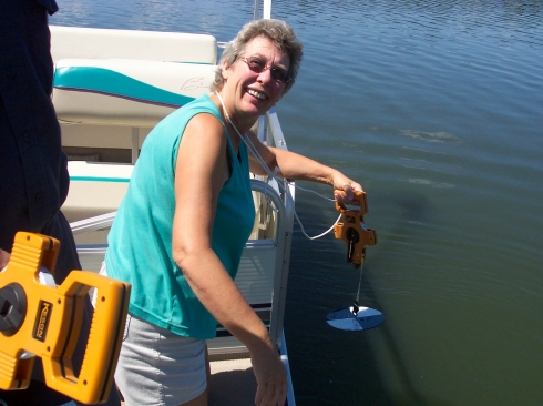 A MiCorps volunteer lowers a patterned Secchi disk into Hicks Lake in Osceola County to measure water clarity. A tape measure is used to determine at what depth the disk is no longer visible.