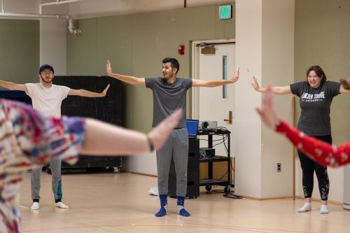 A dance instructor and two MSU students stand in a rehearsal studio with arms outstretched.